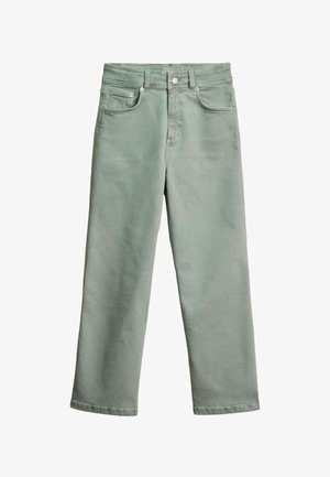 Nő világoszöld, magas derekú, hátsó zsebes farmernadrágot visel, fekete-fehér mintás kötött felsővel, háttal, ezüst mandzsetta karkötőt mutatva.