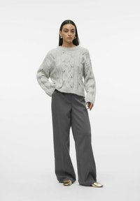 Maglione grigio chiaro a maglia con una vestibilità ampia, abbinato a pantaloni grigi larghi e scarpe slip-on dorate, caratterizzate da un design testurizzato e punti aperti.