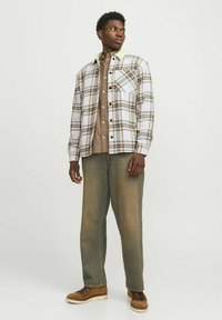Geruite shirt in wit, bruin en beige met een kraag en zakken, gecombineerd met beige broek en bruine laarzen. Gestructureerde stoffen en knoopdetails.