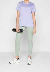 Camiseta deportiva Nike en degradado púrpura, leggings verde menta con costuras laterales, sosteniendo una botella de agua negra, combinados con zapatillas blancas.