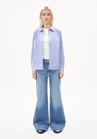 Lichtblauw en wit gestreept overhemd met kraag, gedragen over een wit T-shirt. Gecombineerd met een recht gesneden blauwe spijkerbroek en zwarte sandalen.