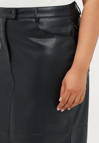 Μαύρη ψεύτικη δερμάτινη φούστα μολύβι με λεία υφή, διαθέτει κλείσιμο με κουμπί, πλαϊνή τσέπη και διακριτές ραφές.