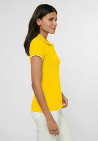 Geel polo-shirt met een slim fit ontwerp, korte mouwen en witte bies langs de kraag en mouwen, gecombineerd met witte broek.