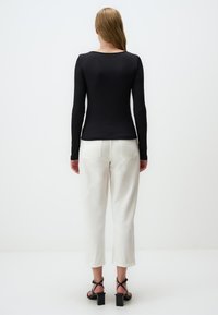 Maglietta nera a costine con maniche lunghe, design aderente, abbinata a pantaloni crema a gamba larga e sandali neri con tacco a blocco. Sfondo semplice.