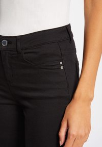Zwarte spijkerbroek van denim met een aansluitend ontwerp, voorzien van een voorzak, decoratieve stikdetails en zilverkleurige hardware accenten bij de taille.