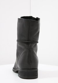 Bota de cuero negro hasta el tobillo con punta redondeada, diseño ligeramente arrugado y tacón bajo apilado. Presenta costuras mínimas y textura suave.