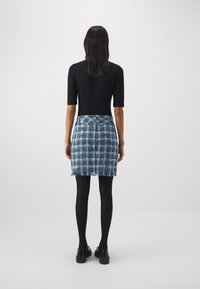 Haut noir à manches courtes associé à une jupe écossaise bleu et verte avec un ourlet à franges, porté avec des collants noirs et des chaussures noires épaisses.