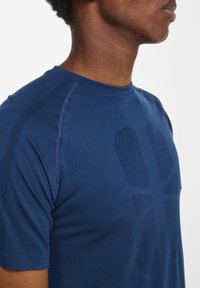 Marinblå sportt-shirt med korta ärmar, strukturerad tyg och ett subtilt grafiskt mönster på framsidan. Rund halsringning och sömlös design.