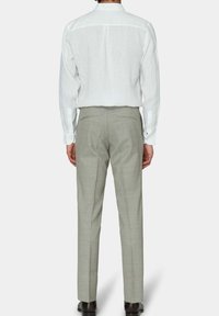 Weißes Leinenhemd mit langen Ärmeln und einem Rückenteil mit Schulterpasse, kombiniert mit hellgrauen maßgeschneiderten Hosen. Das Outfit hat eine schlanke Passform.