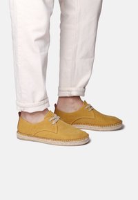 Scarpe di tela gialle con punta rotonda, design con lacci e suola texture. Decoro con un inserto del tallone marrone e dettagli cuciti.