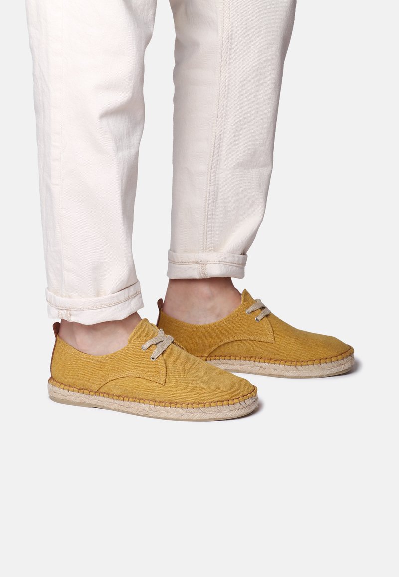 Scarpe di tela gialle con punta rotonda, design con lacci e suola texture. Decoro con un inserto del tallone marrone e dettagli cuciti.