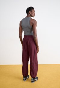 Haut sans manches gris associé à un pantalon bordeaux ample ; le pantalon est doté d'une taille élastique, d'une poche arrière et de chevilles resserrées. Baskets noires.