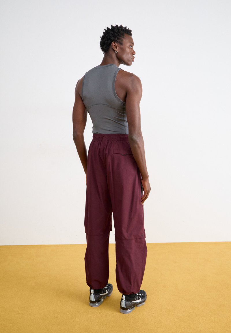 Top gris sin mangas combinado con pantalones burdeos de corte holgado; los pantalones tienen cintura elástica, bolsillo trasero y tobillos ajustados. Zapatillas negras.
