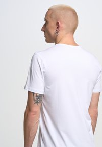 Witte katoenen t-shirt met een ronde hals en korte mouwen. De stof lijkt soepel, met stiksels aan de mouwomslagen.