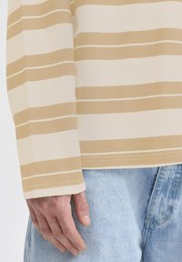 Beige och krämrandig långärmad skjorta med en avslappnad passform, i kombination med ljusblå denimjeans. Har en rak nederkant och synliga sömmar.