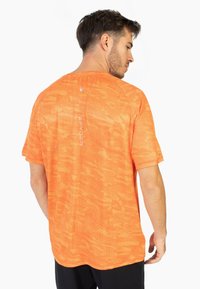 Camiseta atlética naranja con un patrón texturizado, mangas cortas y cuello redondeado. Presenta un logo en la parte posterior y acentos laterales.