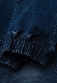Tessuto in denim blu scuro con dettagli di polsino elasticizzato arricciato. La texture è liscia con una leggera sfumatura che indica l'usura. Non sono visibili motivi.