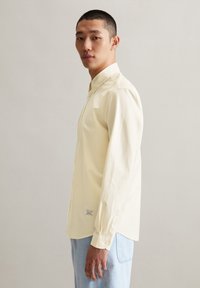 Lichtgele blouse met lange mouwen en verticale strepen, met een button-down kraag en een eenvoudige manchette. Draagt met lichtblauwe jeans, met een label op de zoom.