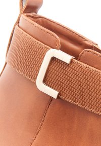 Botte en cuir marron avec une bande tissée texturée, dotée d'un détail de boucle métallique argentée sur le côté, finition lisse et couture renforcée.