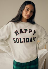 Grå sweatshirt med fet, broderad text som säger "GLAD HÖGTID" i svart med röda detaljer; avslappnad passform, mjuk textur.