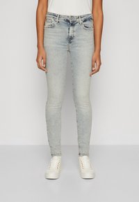 Jeans ajustados de color azul claro, elaborados en denim, con un clásico diseño de cinco bolsillos y un leve desteñido, combinados con zapatillas blancas.