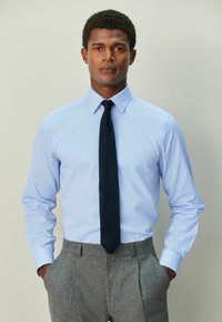 Helesinine triiksärk tekstuurse viimistlusega, millele on lisatud tumesinine lips ja hallid püksid. Omaduseks pikad varrukad ja standardse kaelusega.