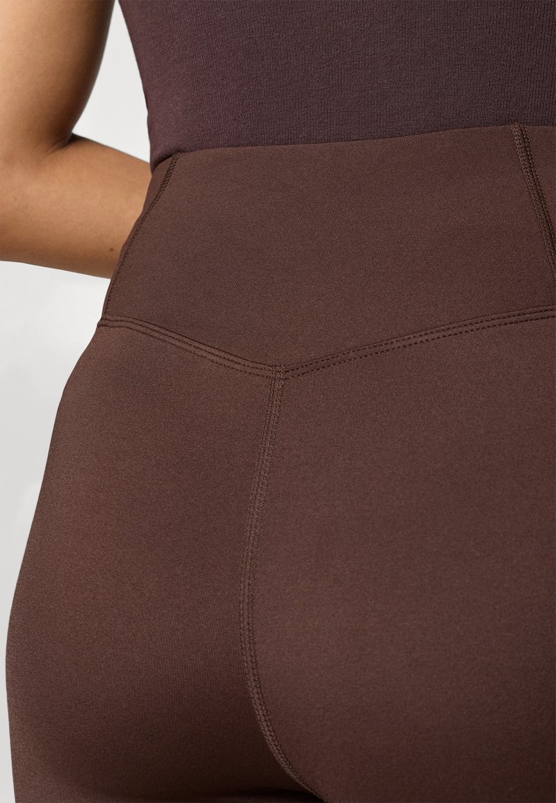 Hoge taille bruine leggings van rekbaar materiaal, met een gladde textuur en dubbeldradige naden voor duurzaamheid.