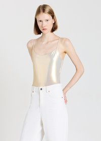 Body metallico dorato con spalline sottili abbinato a jeans bianchi a vita alta, con dettagli di bottoni e tasche. Texture liscia, design riflettente.