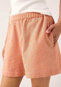 Bomullsshorts i rutigt mönster med orange och vita nyanser. Har en elastisk midja och sidofickor för praktisk användning.