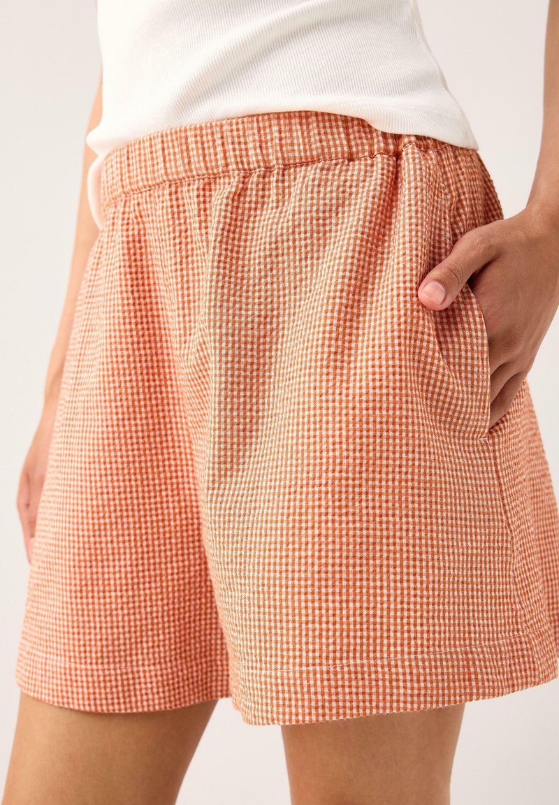 Bomullsshorts i rutigt mönster med orange och vita nyanser. Har en elastisk midja och sidofickor för praktisk användning.