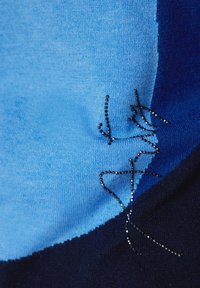 Strickstoff mit einem Verlauf von Hellblau zu Dunkelblau, verziert mit schwarzem Perlenstich, der ein Muster auf der Oberfläche umreißt.