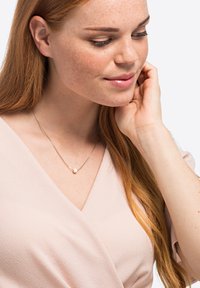 Sølv halskjede med en enkelt perle, båret på en lys rosa omslagstopp. Har en delikat kjede og minimalistisk design. Glatt tekstur.