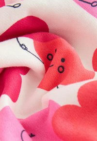 Puuvillakankaan pehmeä pinta, jossa on vaaleanpunaista ja valkoista abstraktia kuviointia sekä mustia viivakorostuksia.