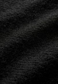 Tissu noir texturé avec une apparence douce et duveteuse. Le matériau présente de fines fibres et une surface légèrement irrégulière.