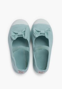 Zapatos slip-on de tela azul claro con suela de goma blanca y un acento de lazo en la parte delantera. Textura suave, diseño minimalista y sin cierre.