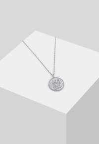 Collana con pendente in argento con un ciondolo circolare che presenta un design dettagliato in rilievo, appesa a una catena attorcigliata, su uno sfondo grigio chiaro.