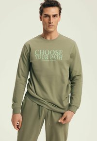 Olive green sweatshirt with long sleeves, crew neckline, and "CHOOSE YOUR PATH" text in light blue. Soft fabric, relaxed fit. Matching pants.