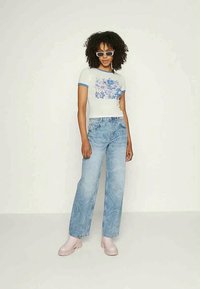 Camisa azul clara com detalhes azul em ringer e gráfico floral, combinada com jeans claros de cintura alta e botas de tornozelo rosas.