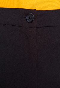 Pantalon noir à texture lisse, doté d'un seul bouton noir à la taille et d'une silhouette propre et ajustée.