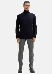 Ciemnogranatowy sweter z golfem o prążkowanej fakturze, zestawiony z jasnoszarymi spodniami i czarnymi botkami za kostkę, o prostym kroju i dopasowanej formie.