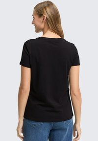 Zwart T-shirt met korte mouwen en een ronde hals, zachte textuur en een getailleerd ontwerp. Draag het met blauwe spijkerbroeken.