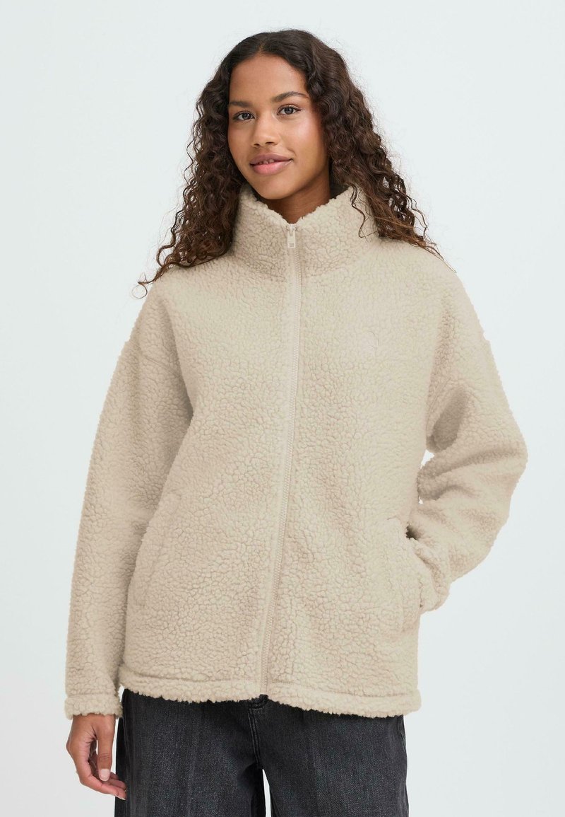 Beežist fliisist jope kõrge krae, esikinnituse ja küljetaskutega. Omadusteks on tekstureeritud, pehme pind ja lõdvestunud lõige.