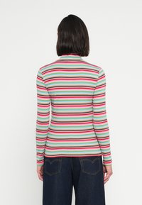 Bluza cu mâneci lungi cu dungi în tonuri de teal, roz, roșu, maro și alb. Croială strâmtă, cu guler înalt și textură rilată. Asortată cu pantaloni din denim închis la culoare.