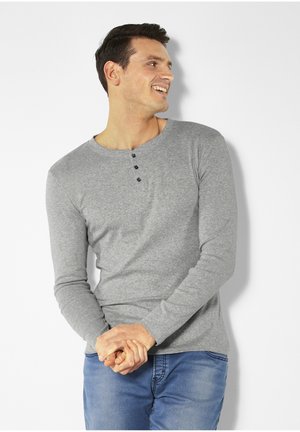 Graues Langarmshirt aus weichem Stoff mit einem weit ausgeschnittenen Ausschnitt und drei schwarzen Knöpfen, kombiniert mit lässigen blauen Jeans.