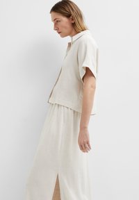 Linen shirt and skirt set in light beige. Shirt features a short, loose sleeve and a collar. Skirt has a front slit, offering a relaxed silhouette.