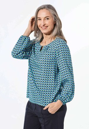 Blaue Bluse mit geometrischen Dreiecken in Grün und Marineblau. Sie hat einen runden Ausschnitt und lange, geraffte Ärmel. Weicher Stoff.