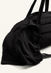 Geantă de voiaj din pânză neagră, cu închidere cu șnur strâns, laturi texturate și două mânere rezistente. Design compact, moale și aerodinamic.