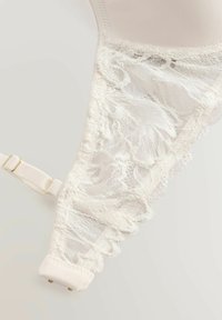 Reggiseno bianco con dettagli in pizzo sui lati, realizzato in tessuto morbido, con spalline regolabili e una superficie liscia con bordo a scallop.