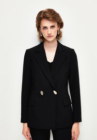 Černý dvouřadý blazer s klopami, dvěma předními kapsami a knoflíky v stříbrném tónu. Přizpůsobený střih s hladkou texturou.