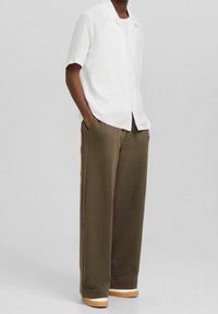 Camicia bianca a maniche corte con colletto, abbinata a pantaloni beige larghi e sneakers chiare, con tasche laterali.